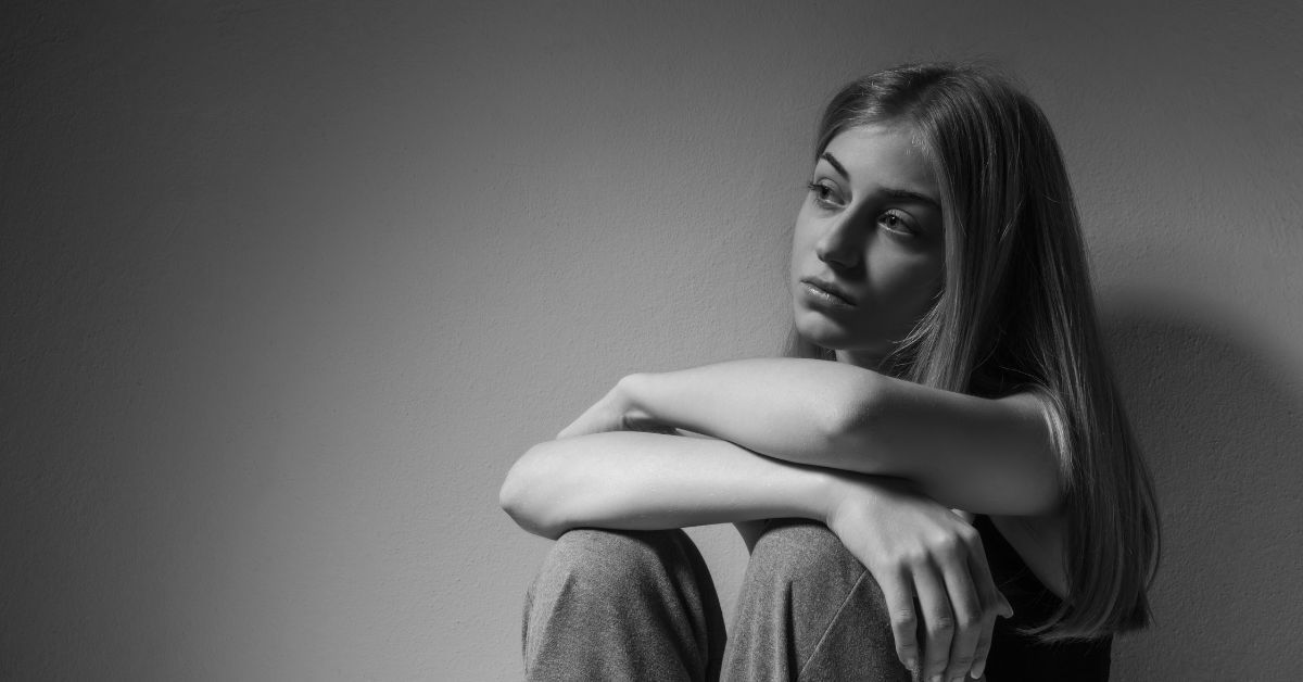 A black and white photo of a young woman sitting on the floor with her legs crossed.