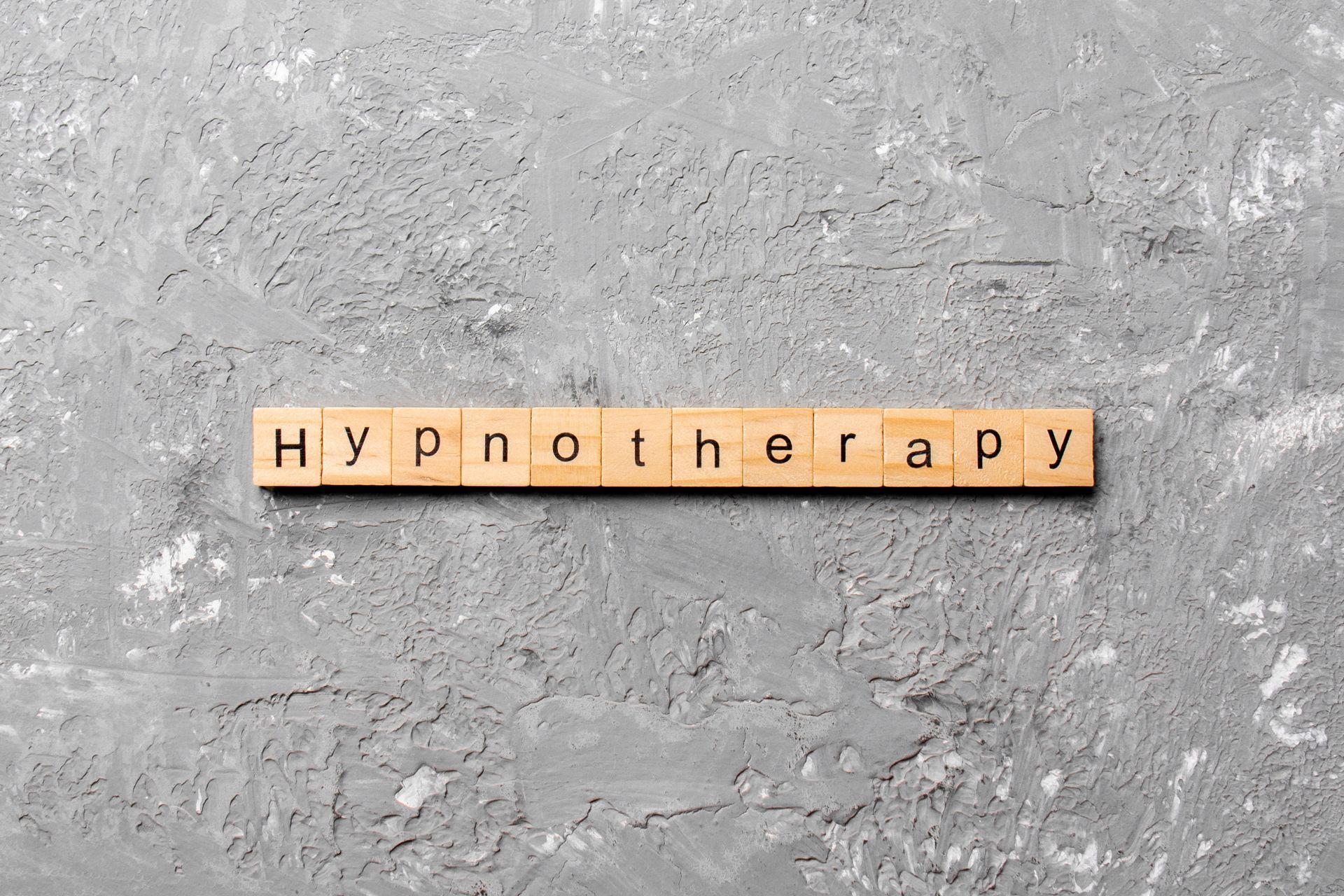 The word hypnotherapy is written on wooden tiles on a gray background.