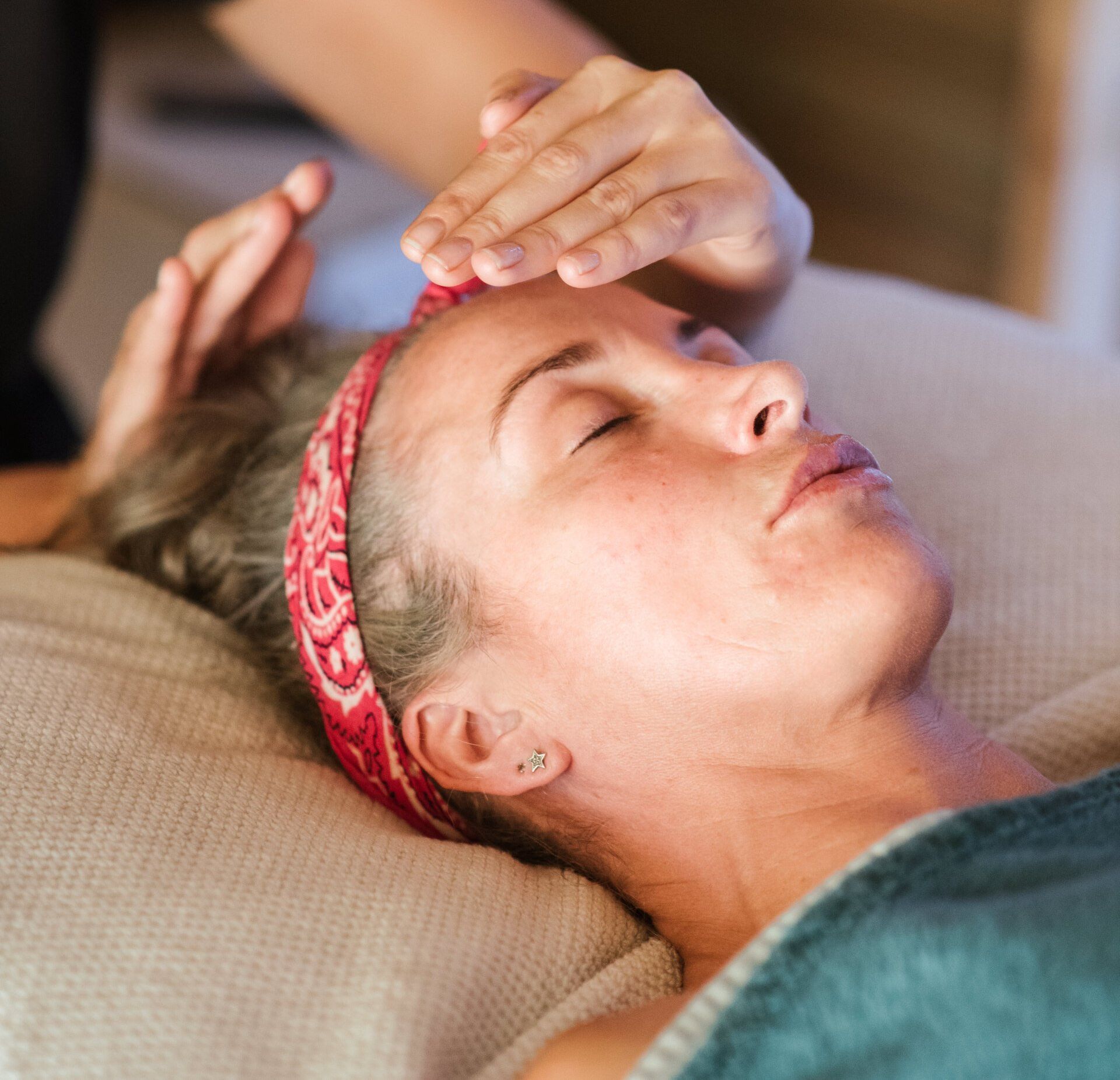 A woman wearing a red headband is getting a massage on her forehead.