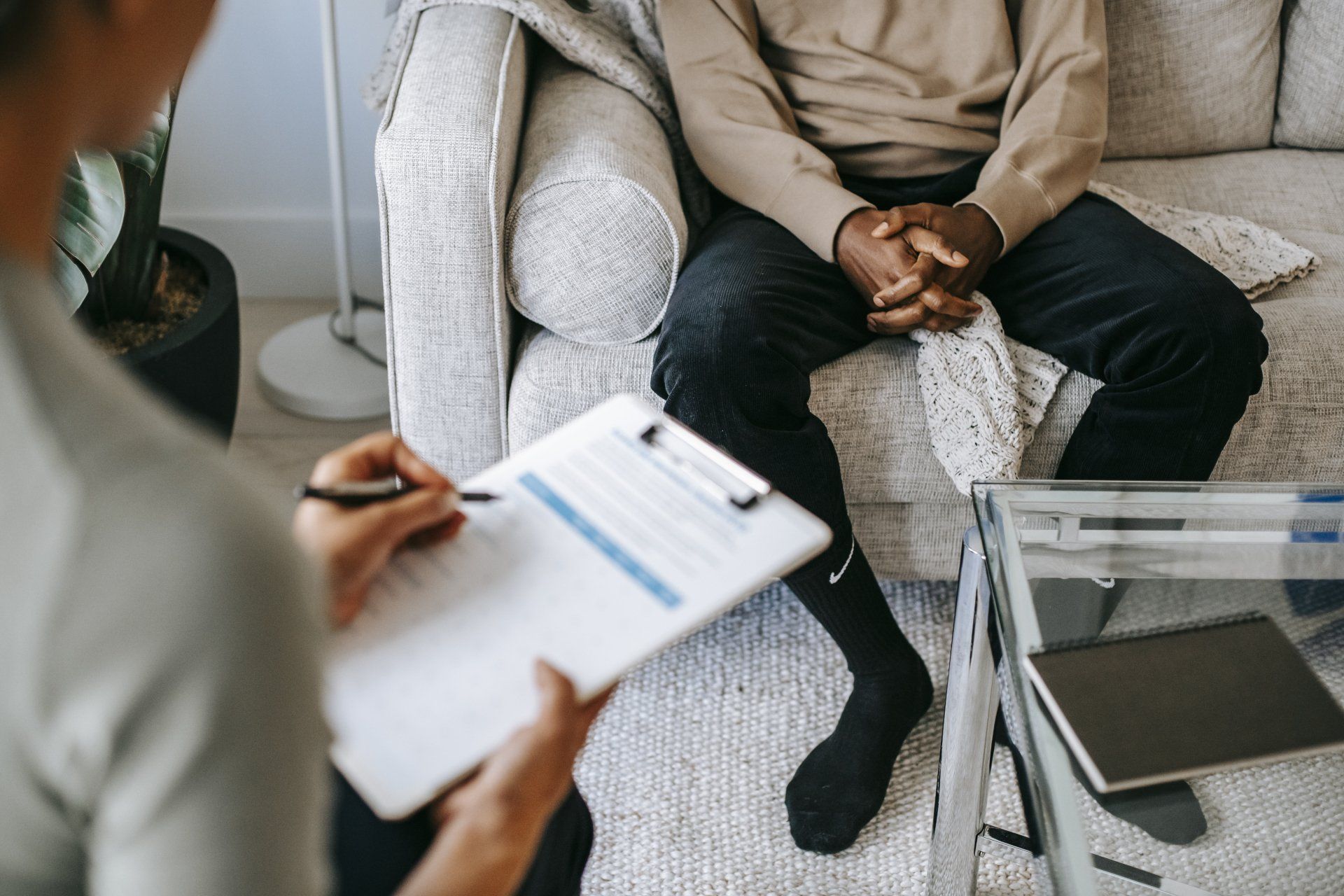 A man is sitting on a couch while a woman holds a clipboard.