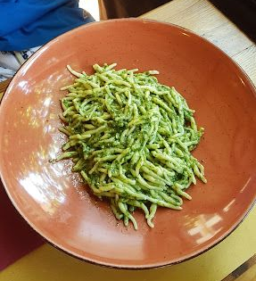Pasta al pesto in una ciotola color terracotta su un tavolo di legno.