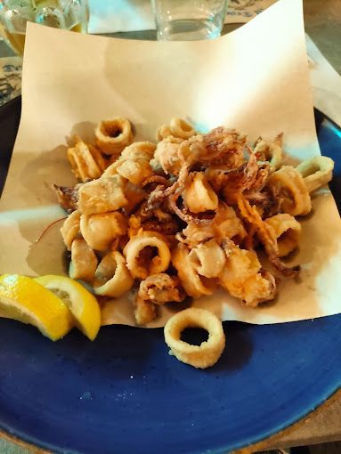 Anelli e tentacoli di calamari fritti su un piatto rivestito di carta con spicchi di limone.