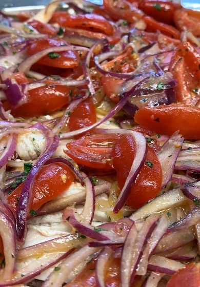 Insalata di pomodori e cipolle rosse, con erbe aromatiche a vista, con condimento leggero.