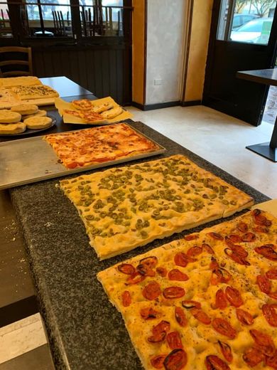 Pizza esposta su un bancone, con vari condimenti come pomodori ed erbe aromatiche, all'interno.