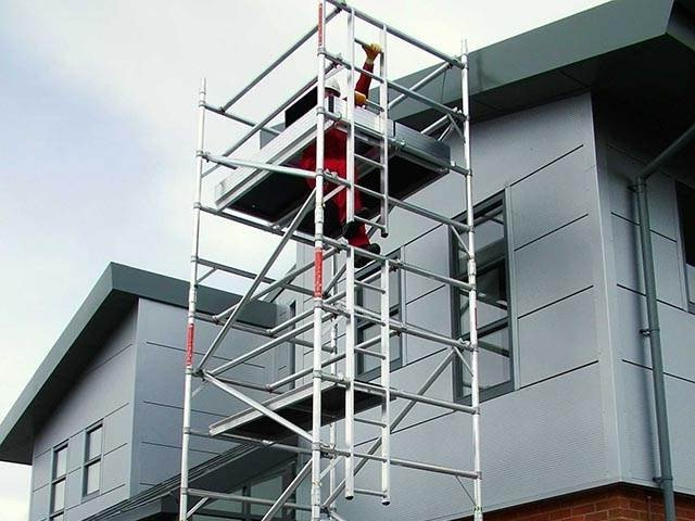 A man is working on a scaffold in front of a residential building.