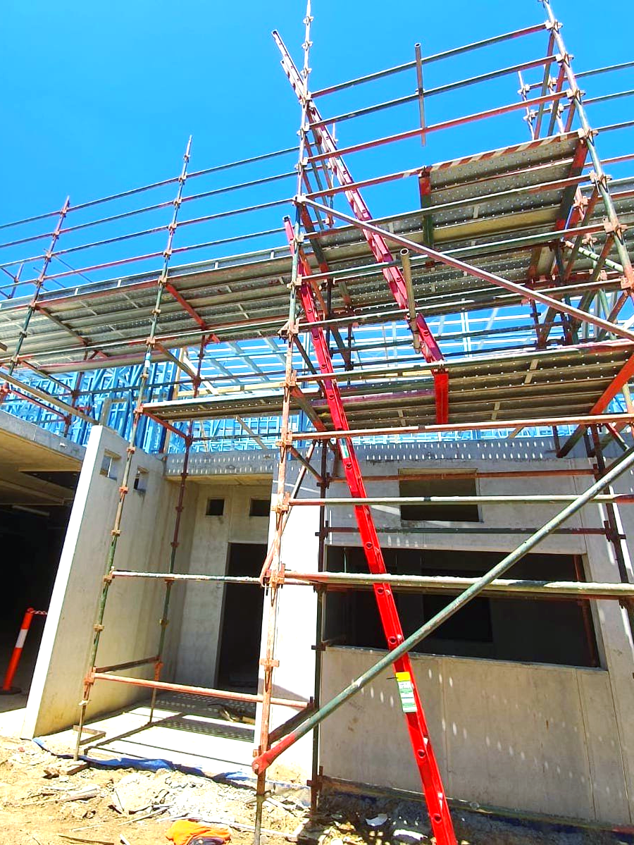 A building under construction with scaffolding and a red ladder.