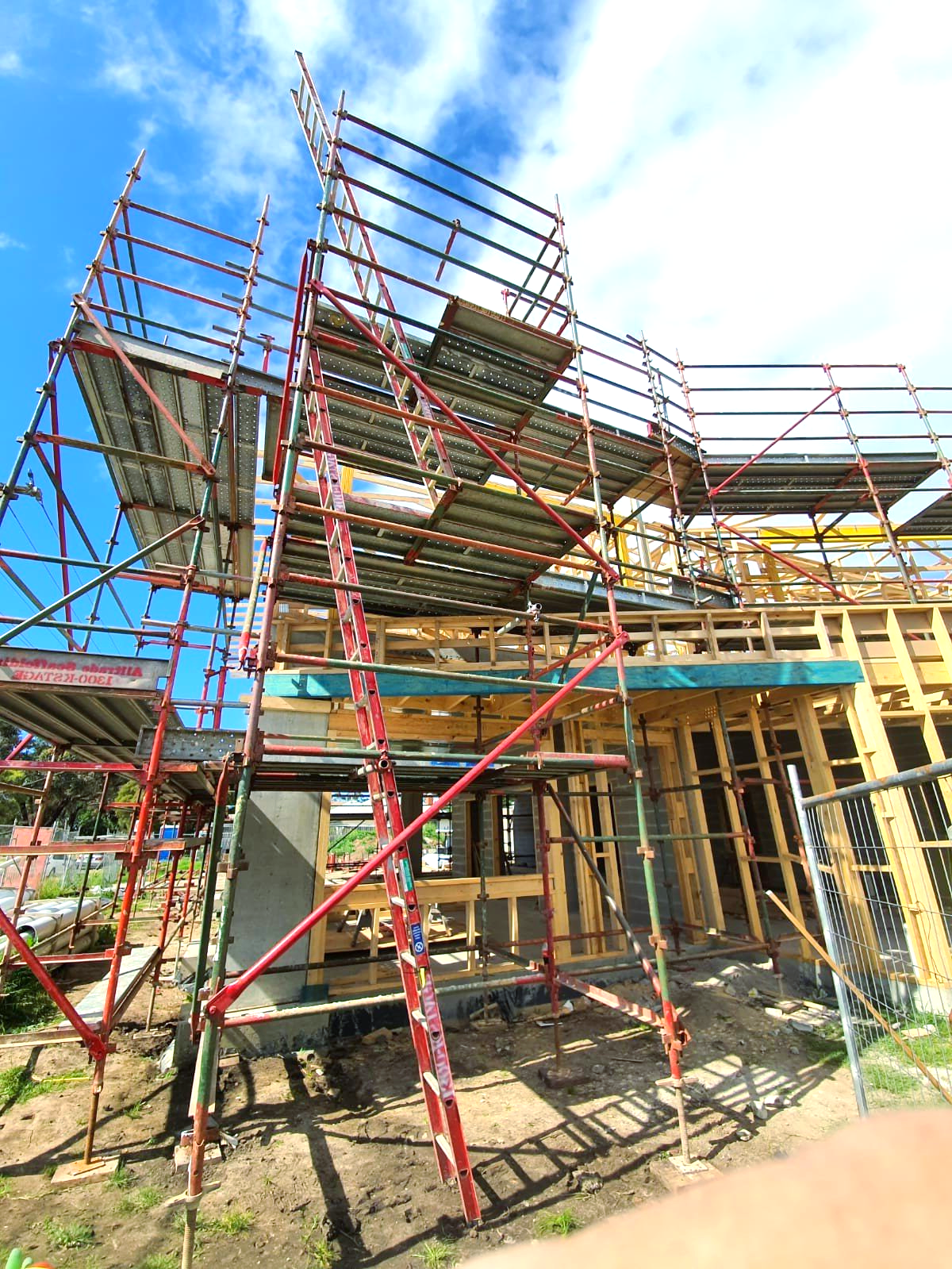 A building under construction with scaffolding and a red ladder.