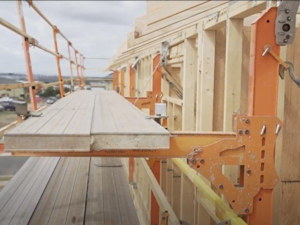 Construction workers using orange scaffolding, boards, and safety rails at a building site.