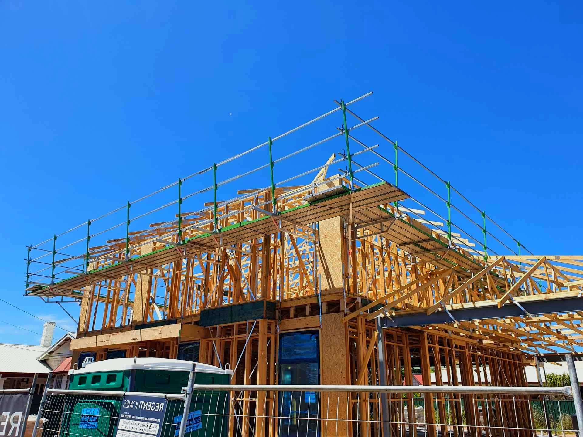 Construction site with wooden frame building, scaffolding, and a clear blue sky.