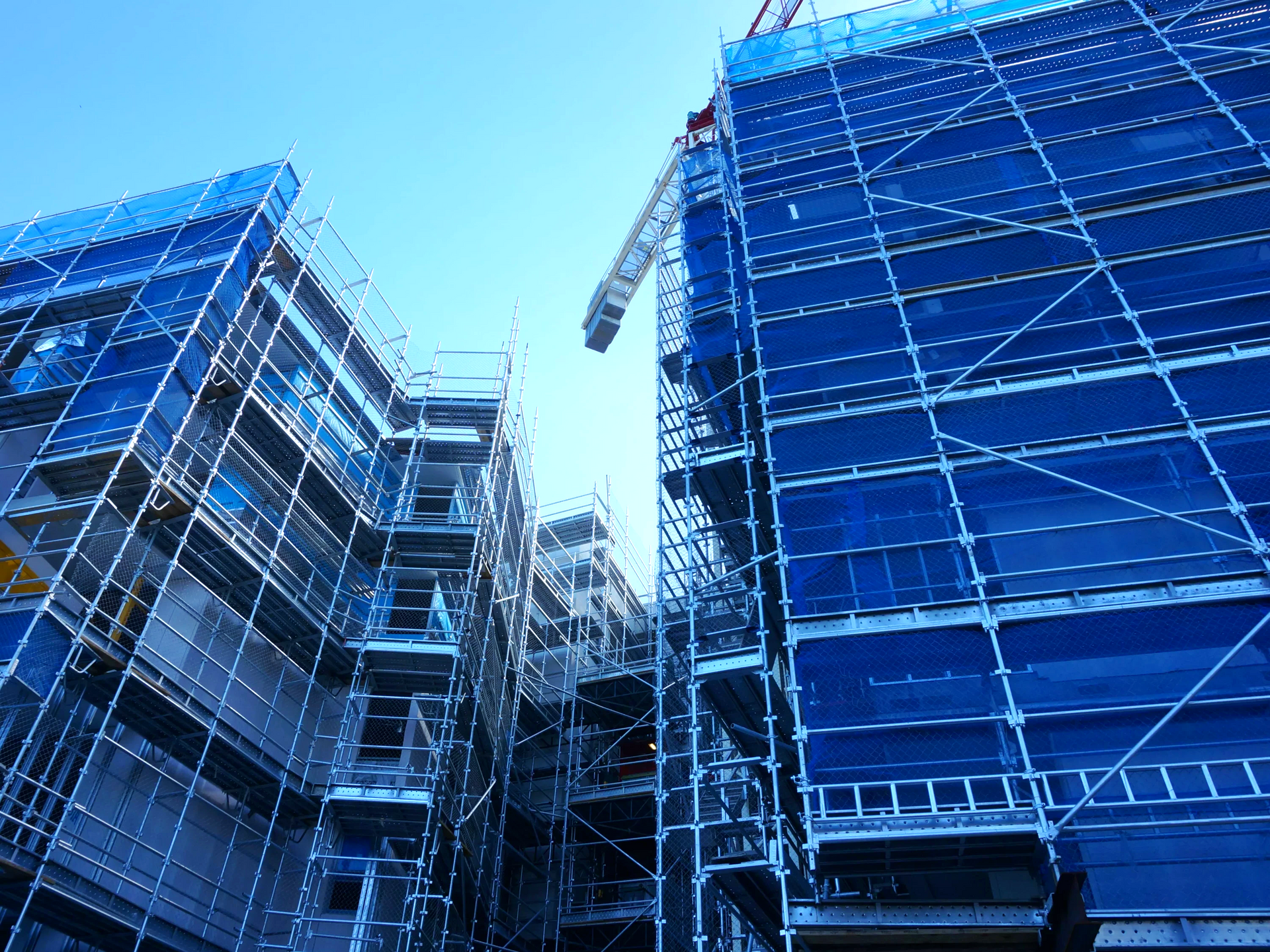 A building under construction with blue scaffolding and a crane.