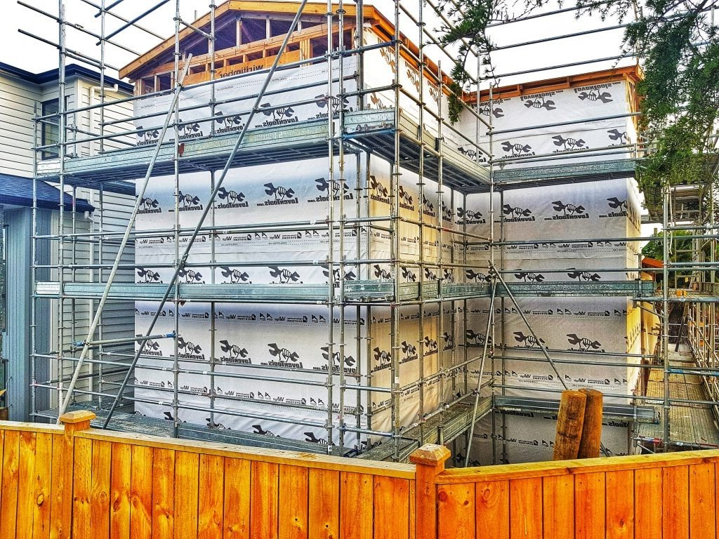 A house is being built with scaffolding around it and a wooden fence.