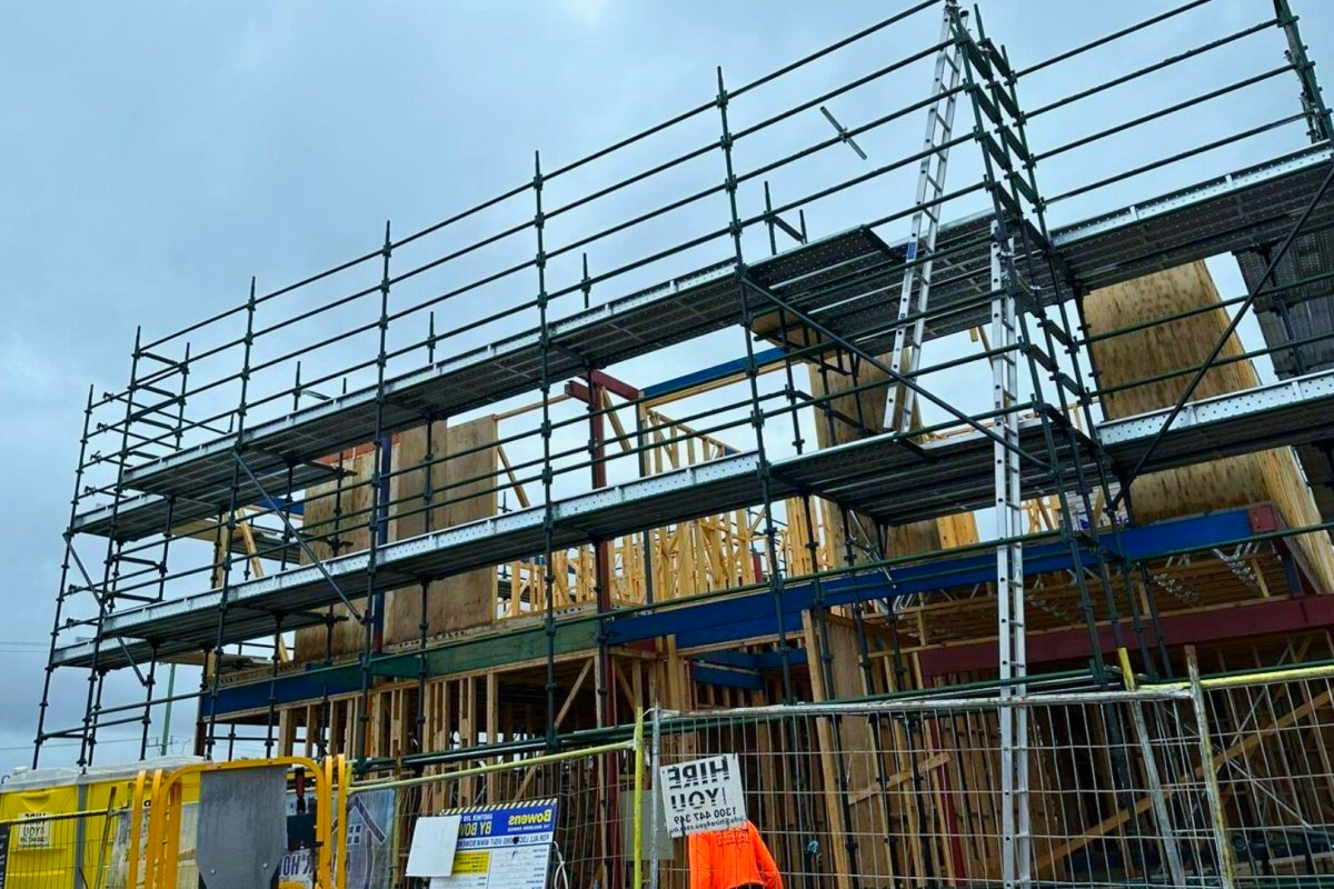 Scaffolding surrounds a building under construction. Cloudy sky, wooden frame, safety fence in foreground.