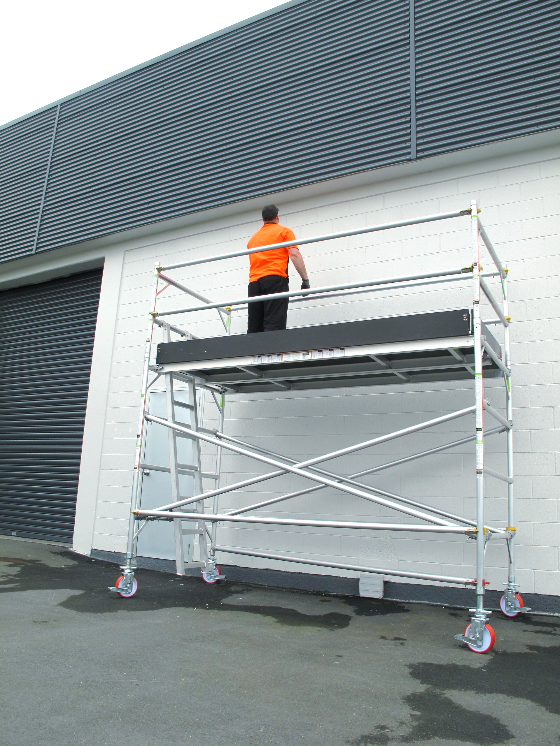 A man is standing on a scaffolding in front of a building.