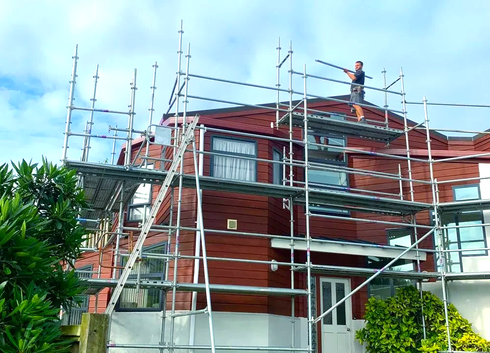 A man is standing on a scaffolding on top of a house.