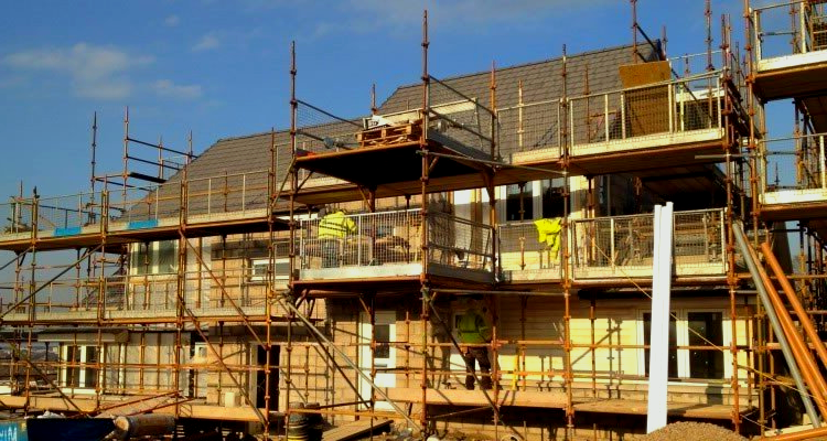 Construction of a multi-story building with scaffolding and workers in yellow vests on a sunny day.