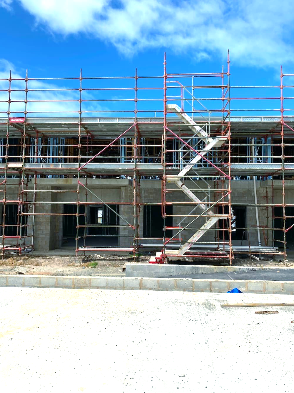 Construction scaffolding in front of a concrete building under a bright blue sky.