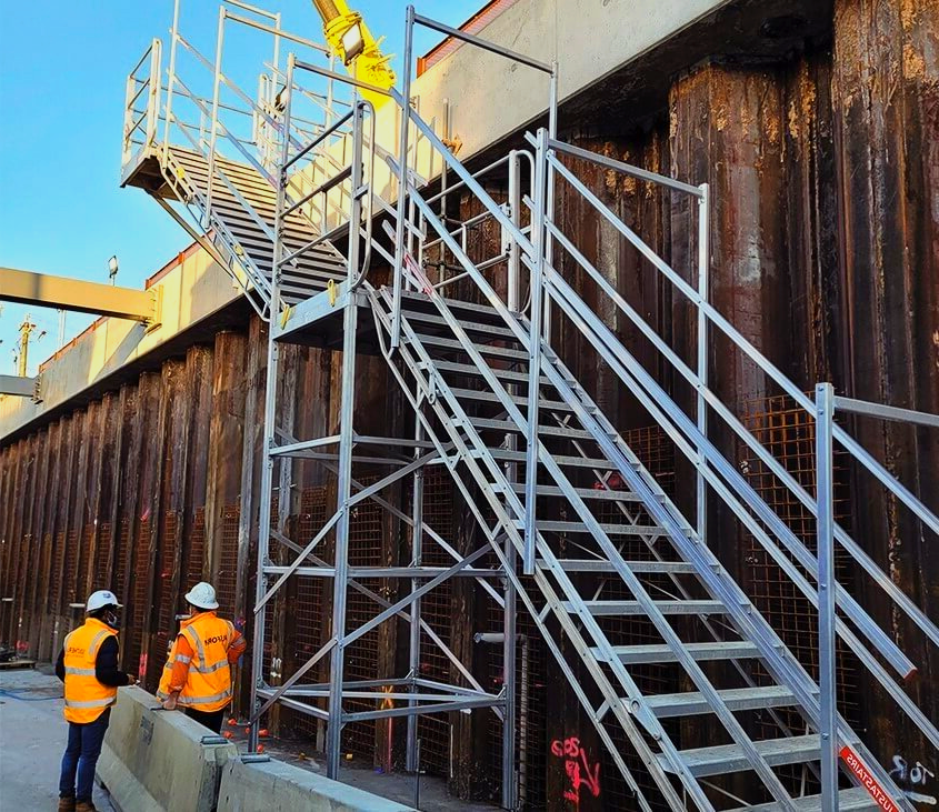 Two construction workers are standing next to a set of stairs.