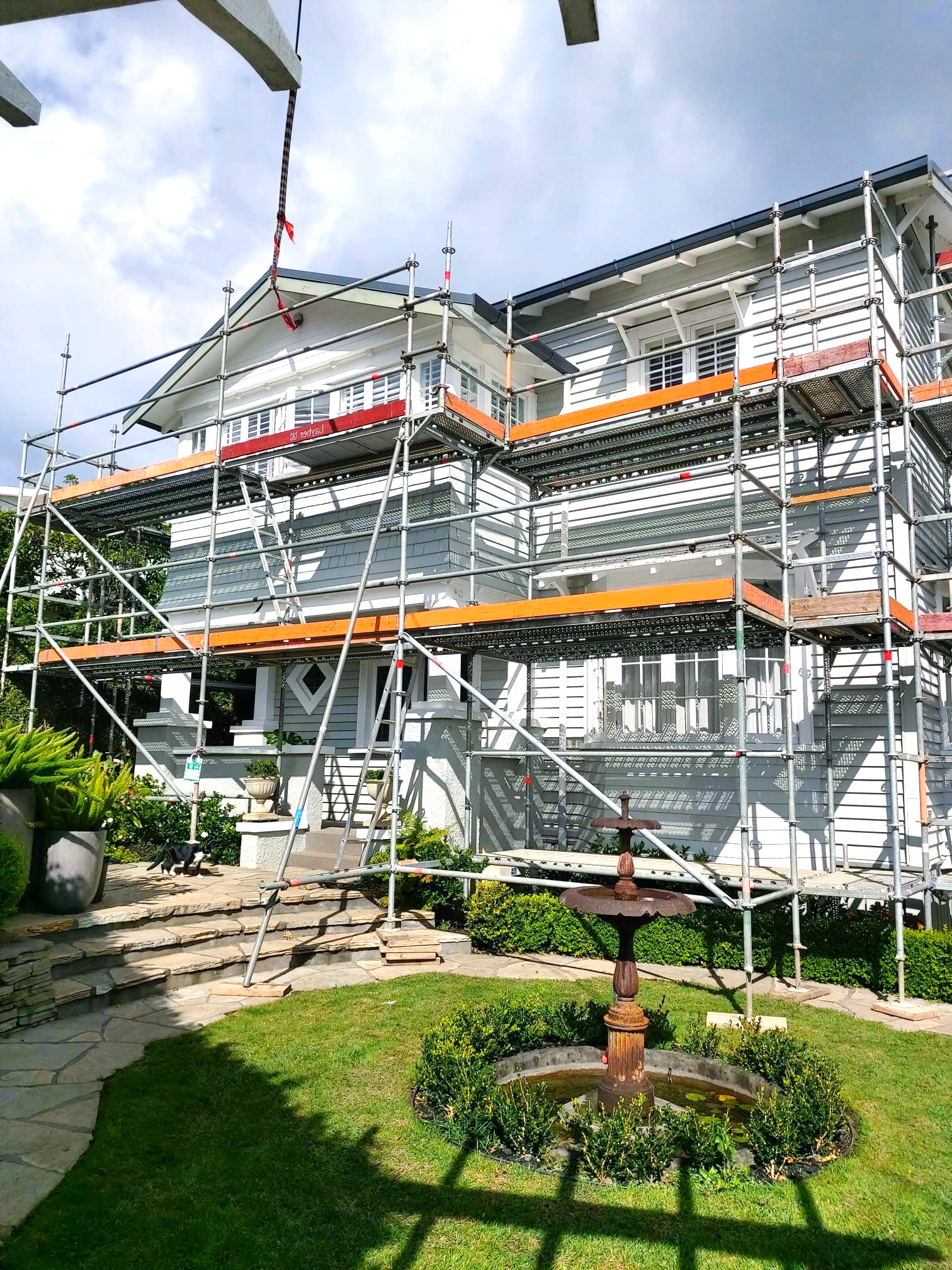 A large white house with scaffolding around it and a fountain in front of it.
