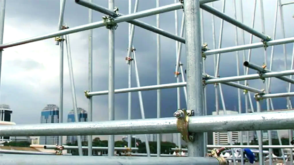 A scaffolding structure made of metal pipes with a cloudy sky in the background.