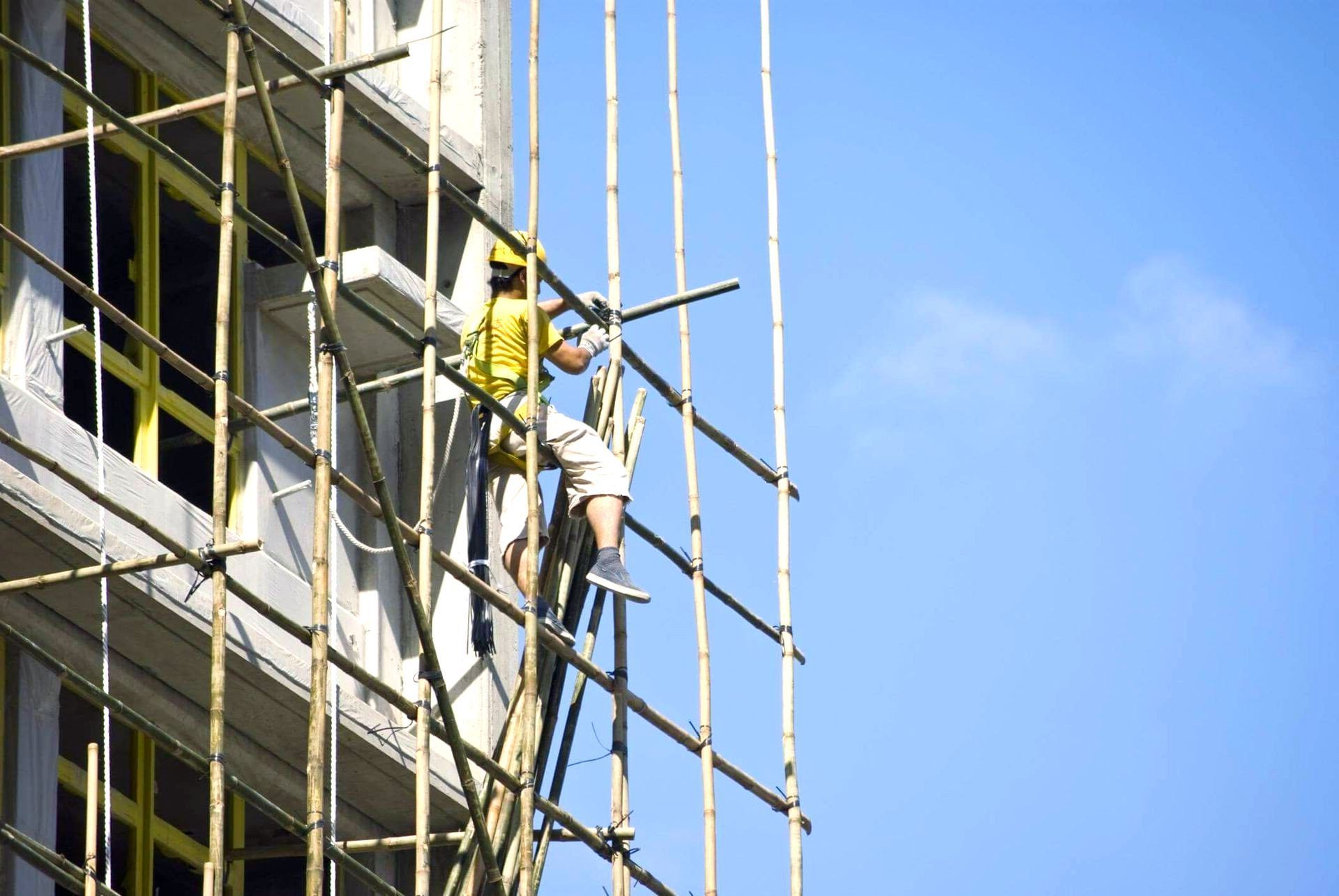 A man in yellow helmet working on a scaffolding on the side of a building.