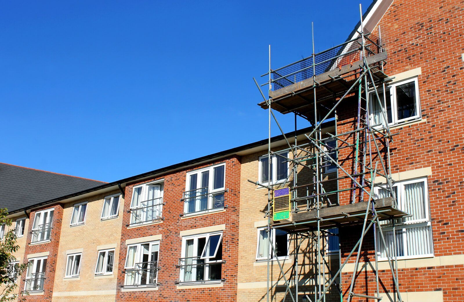 a two to three storey orange and brown brick building with scaffolding in front of part of it.