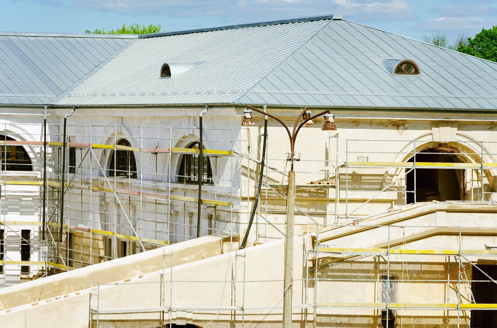 Building exterior under renovation, with scaffolding, arched windows, and a metal roof.