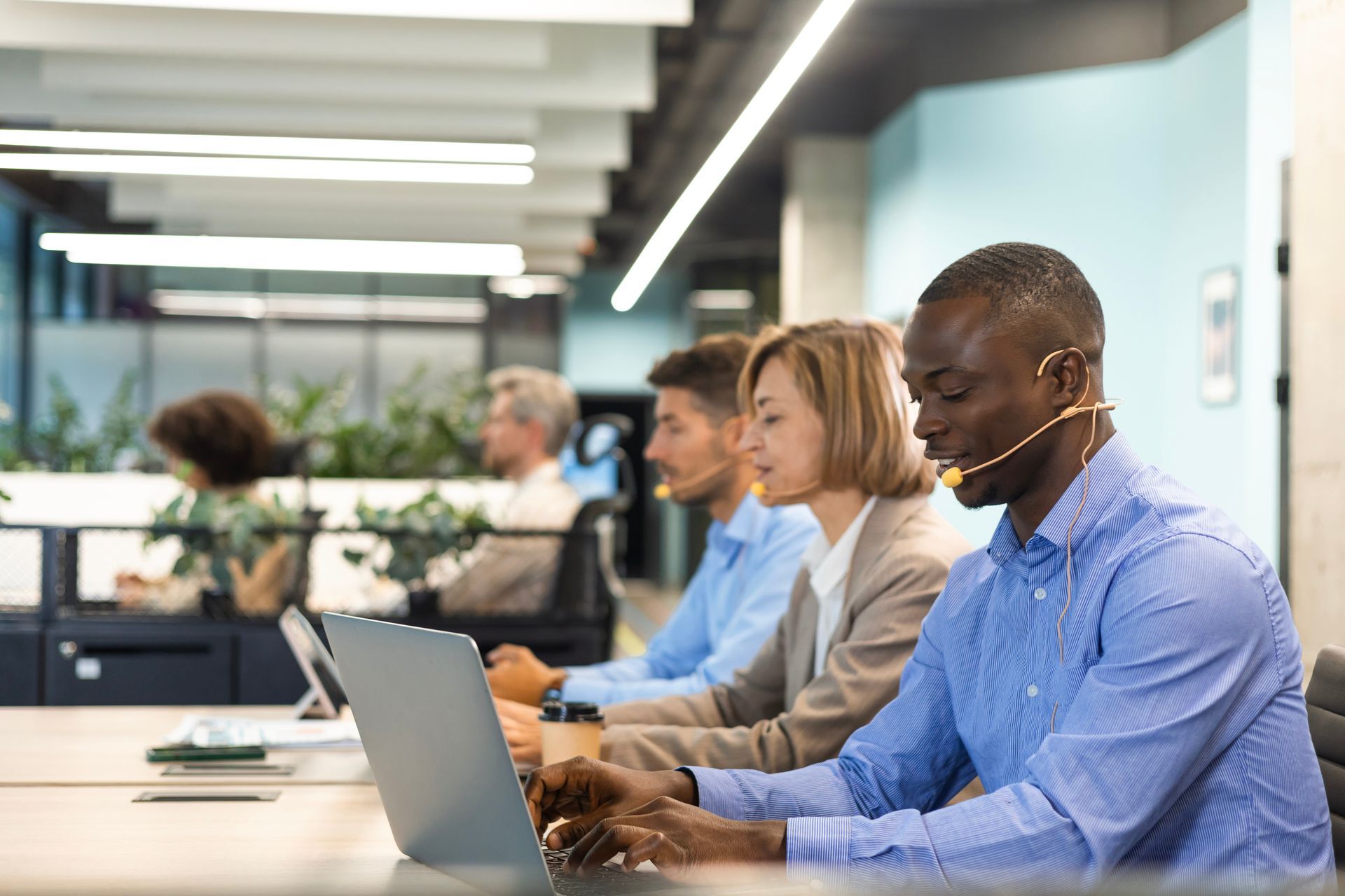 A man wearing a headset is using a laptop computer in a call center.