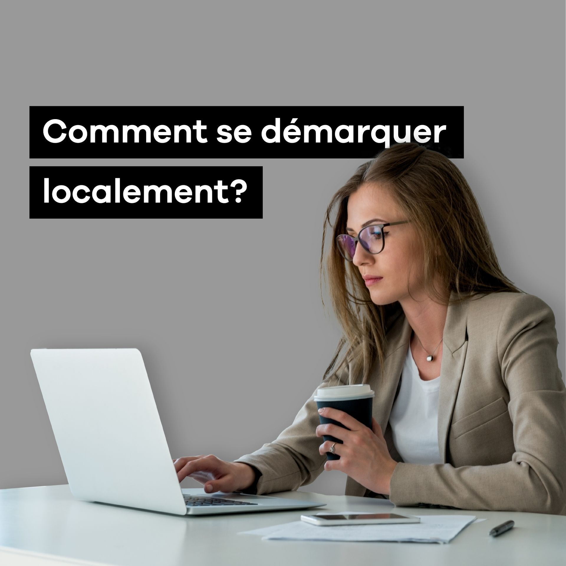 Une femme est assise à un bureau en utilisant un ordinateur portable tout en tenant une tasse de café.