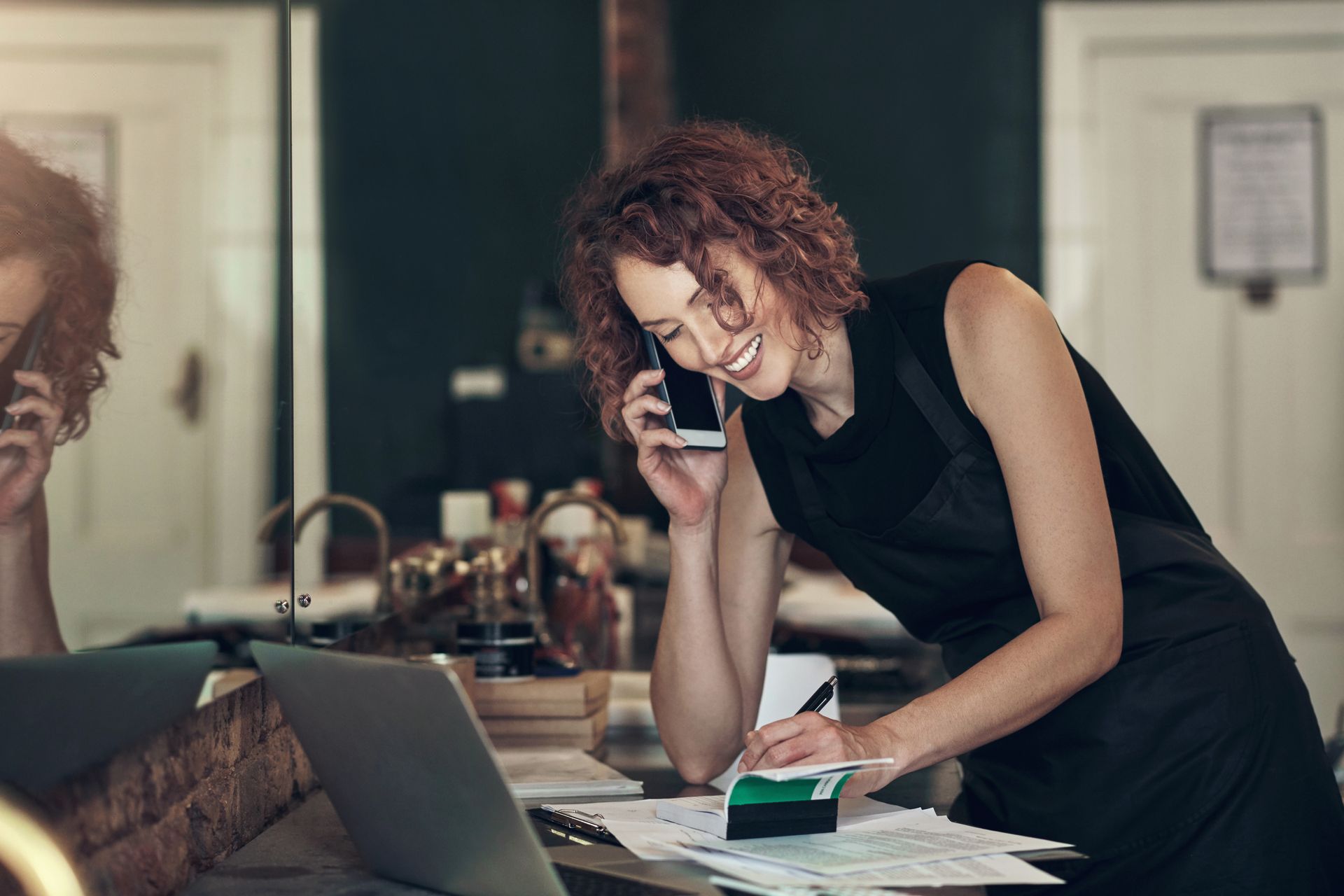 A woman is talking on a cell phone while looking at a laptop.