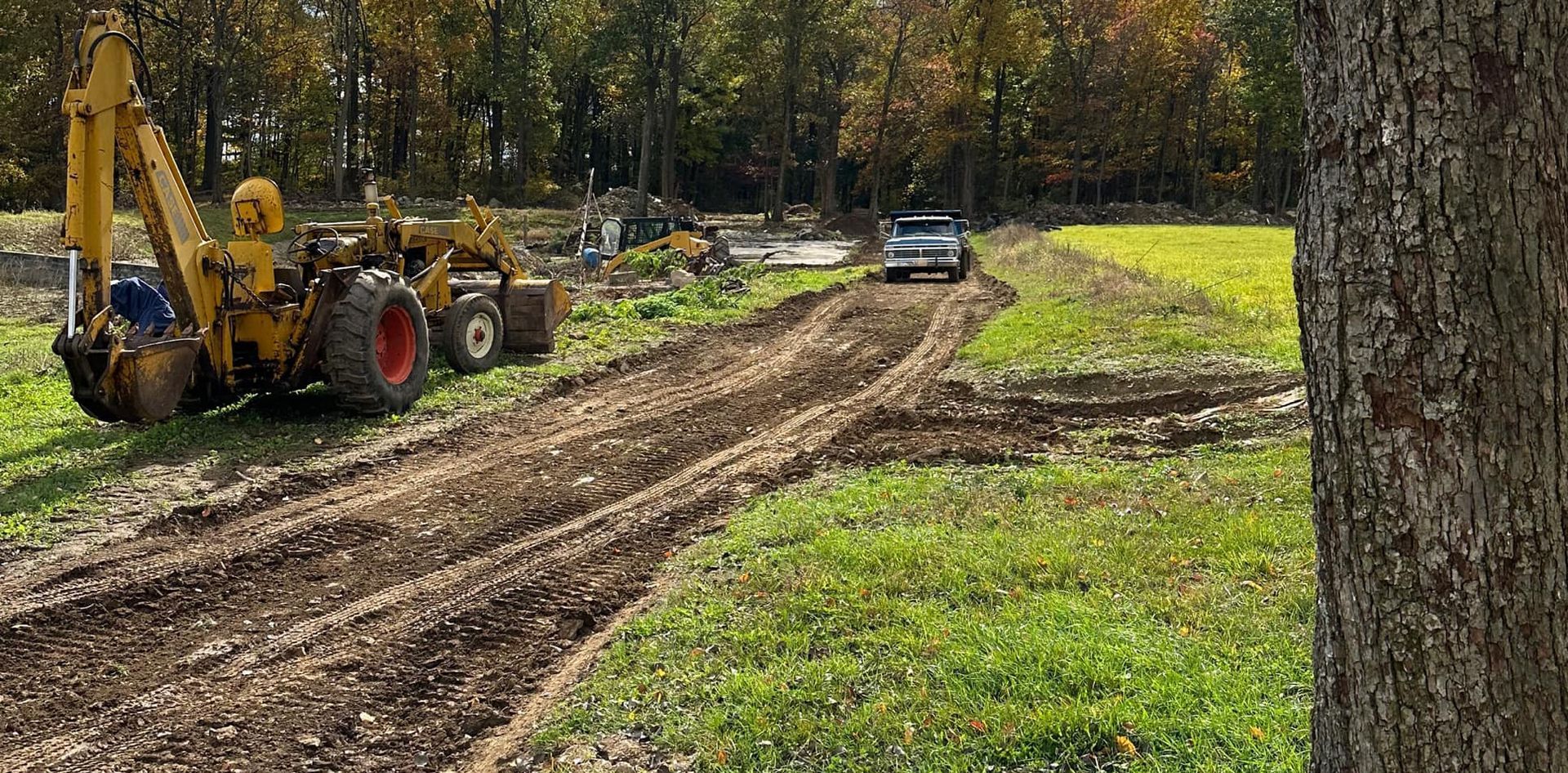 A yellow tractor is driving down a dirt road next to a tree.