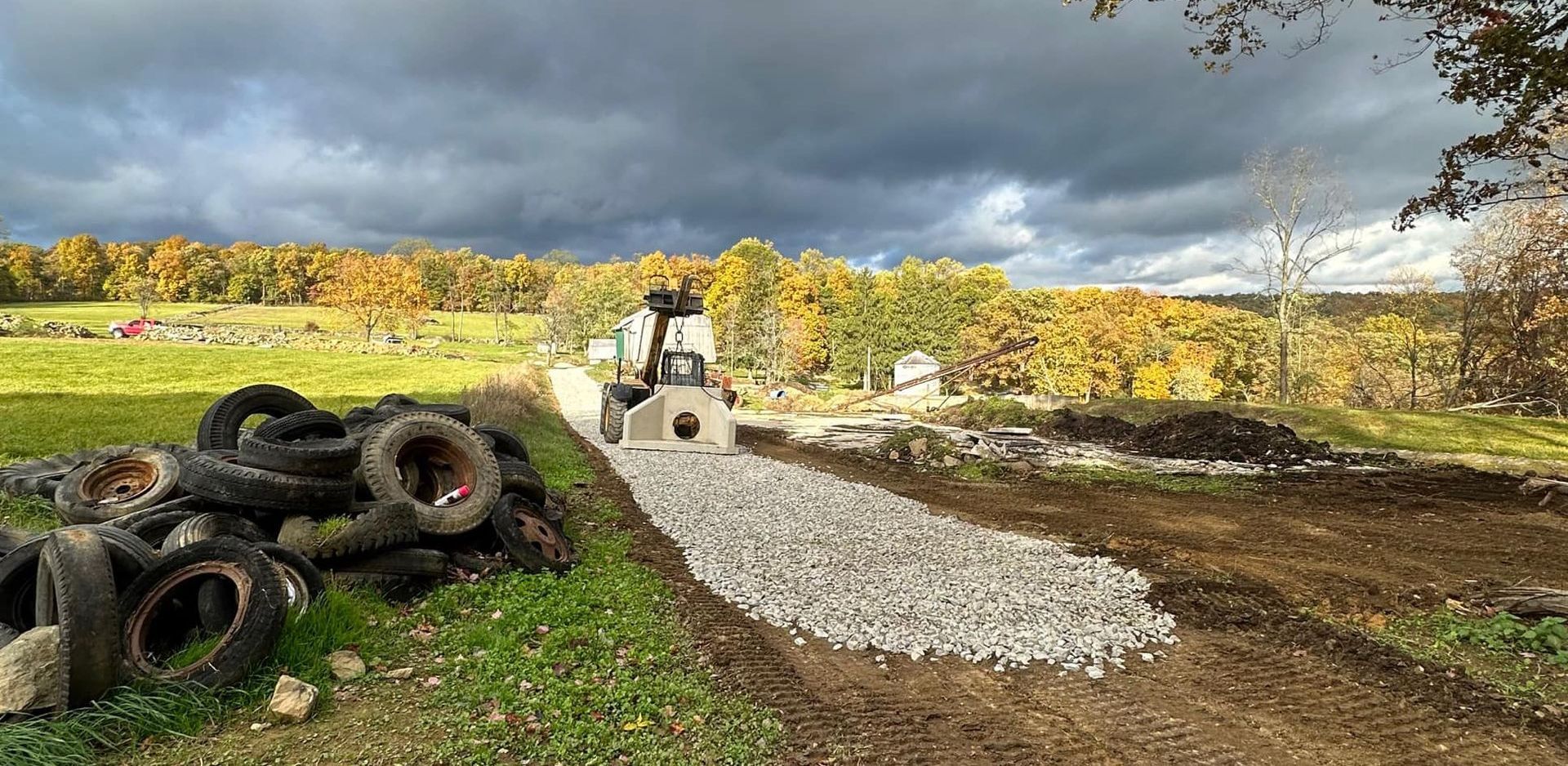 A tractor is driving down a dirt road next to a pile of tires.