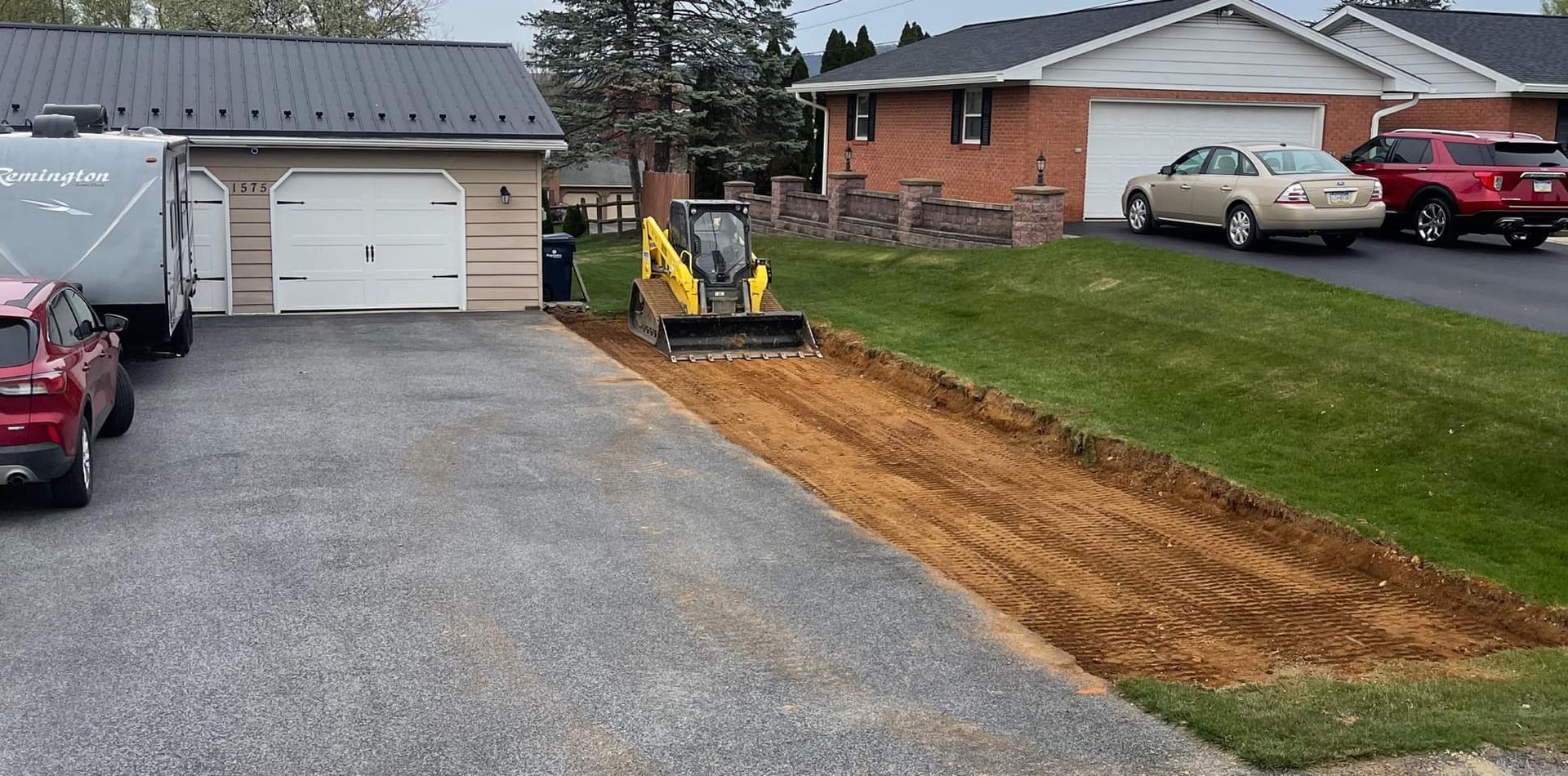 A yellow excavator is working on a driveway next to a house.
