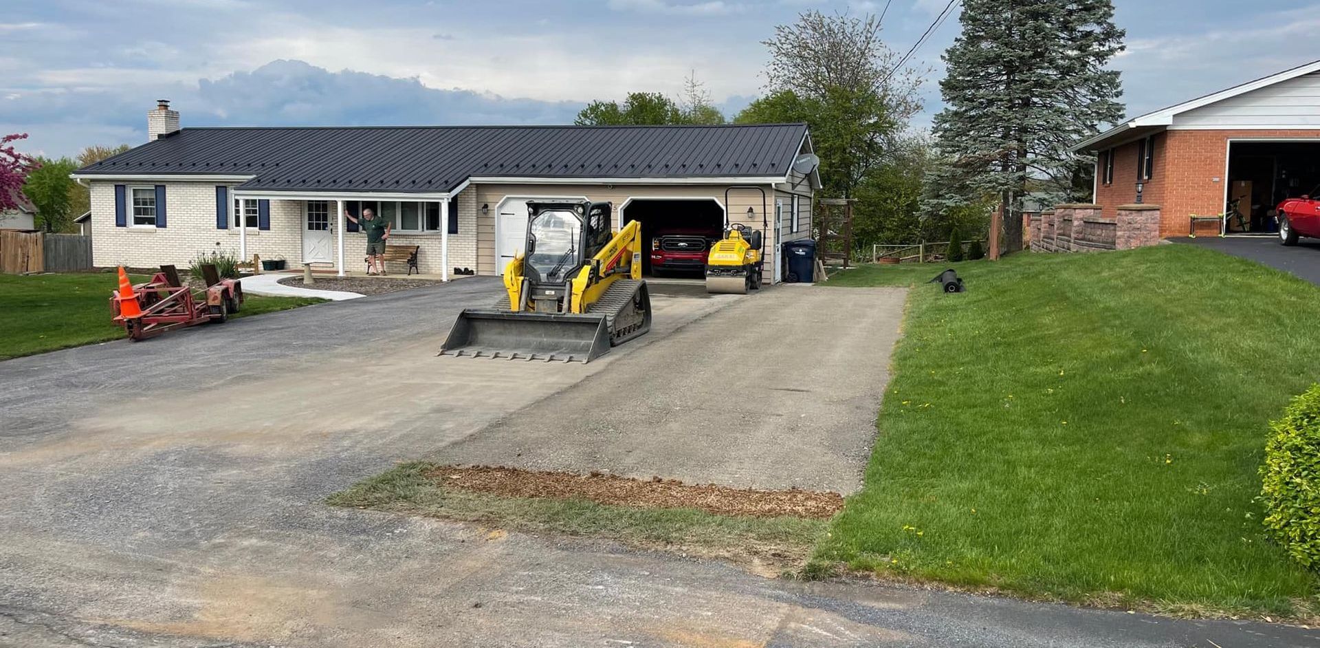 A bulldozer is driving down a dirt road in front of a house.