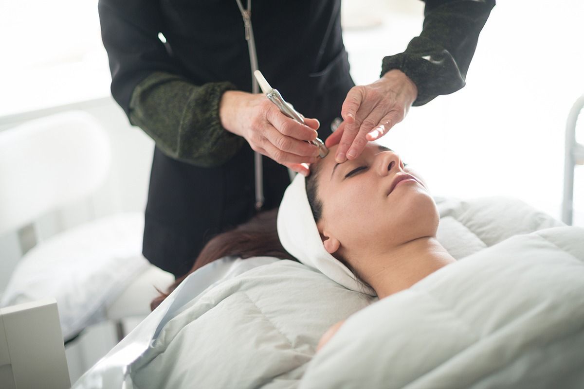 Woman receiving facial treatment; esthetician using a tool on her forehead.