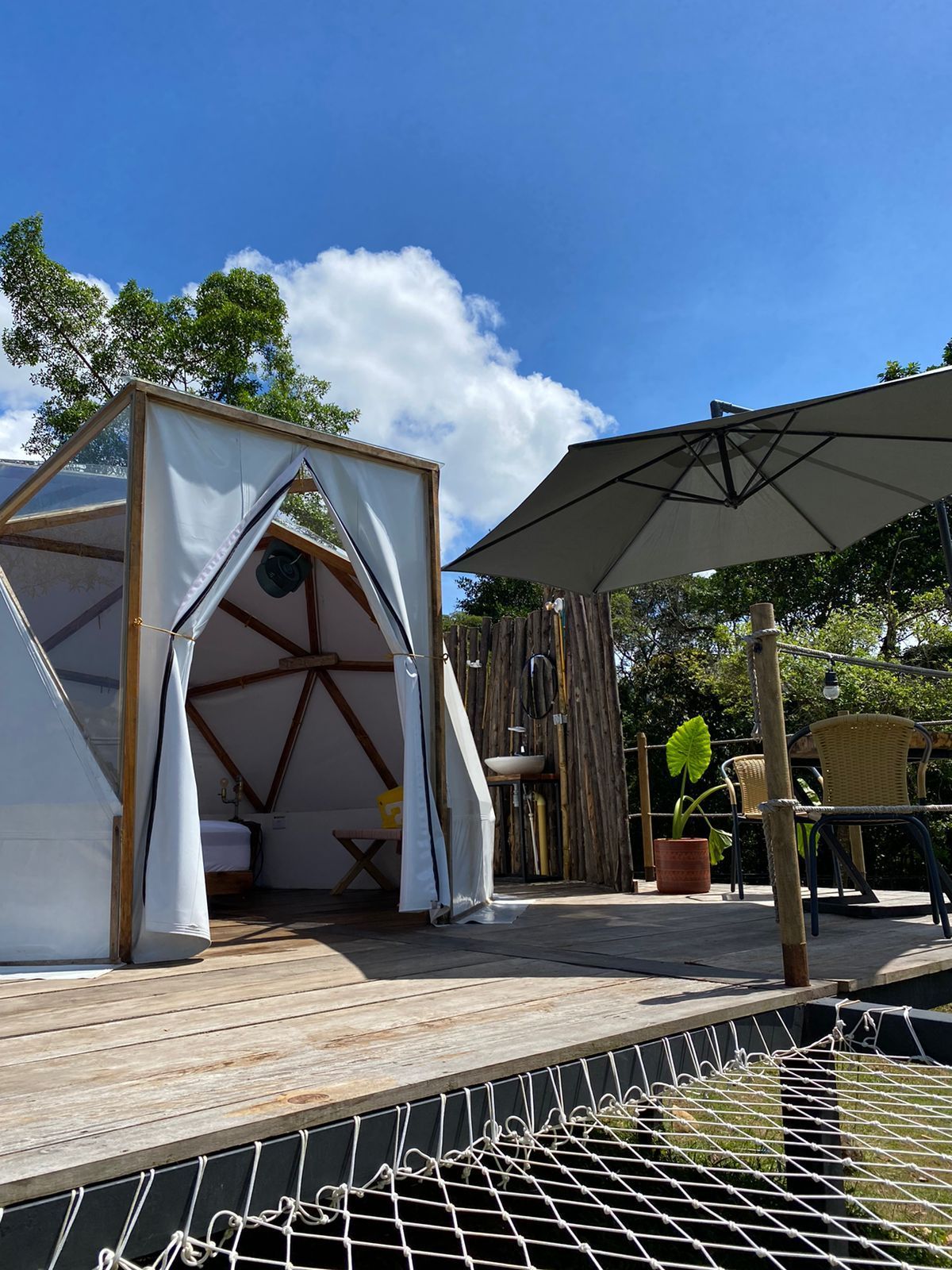 Estructura glamping con cúpula geodésica y zona de estar al aire libre bajo un cielo azul.