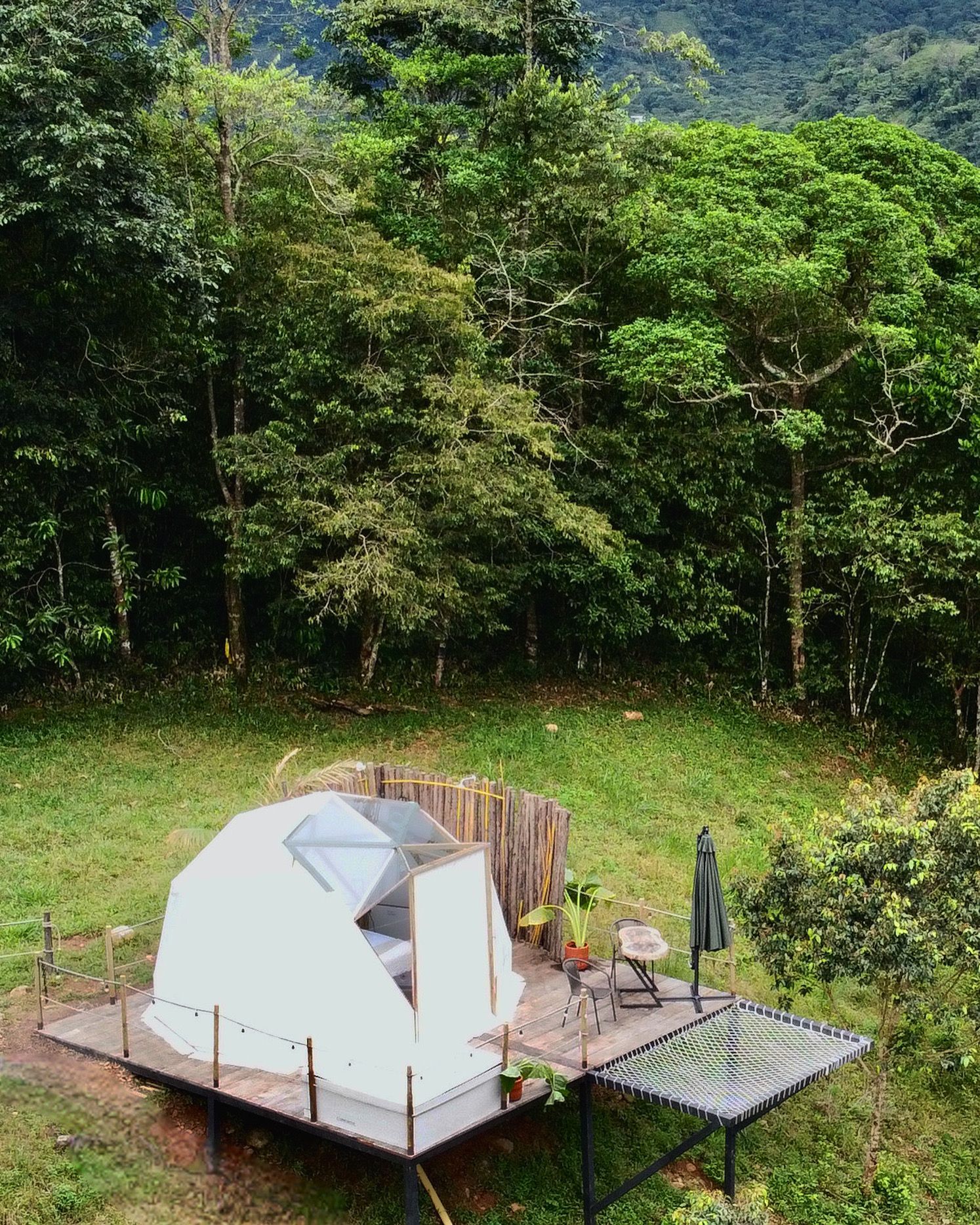 Tienda glamping con cúpula geodésica blanca sobre una plataforma de madera en un entorno de bosque verde.