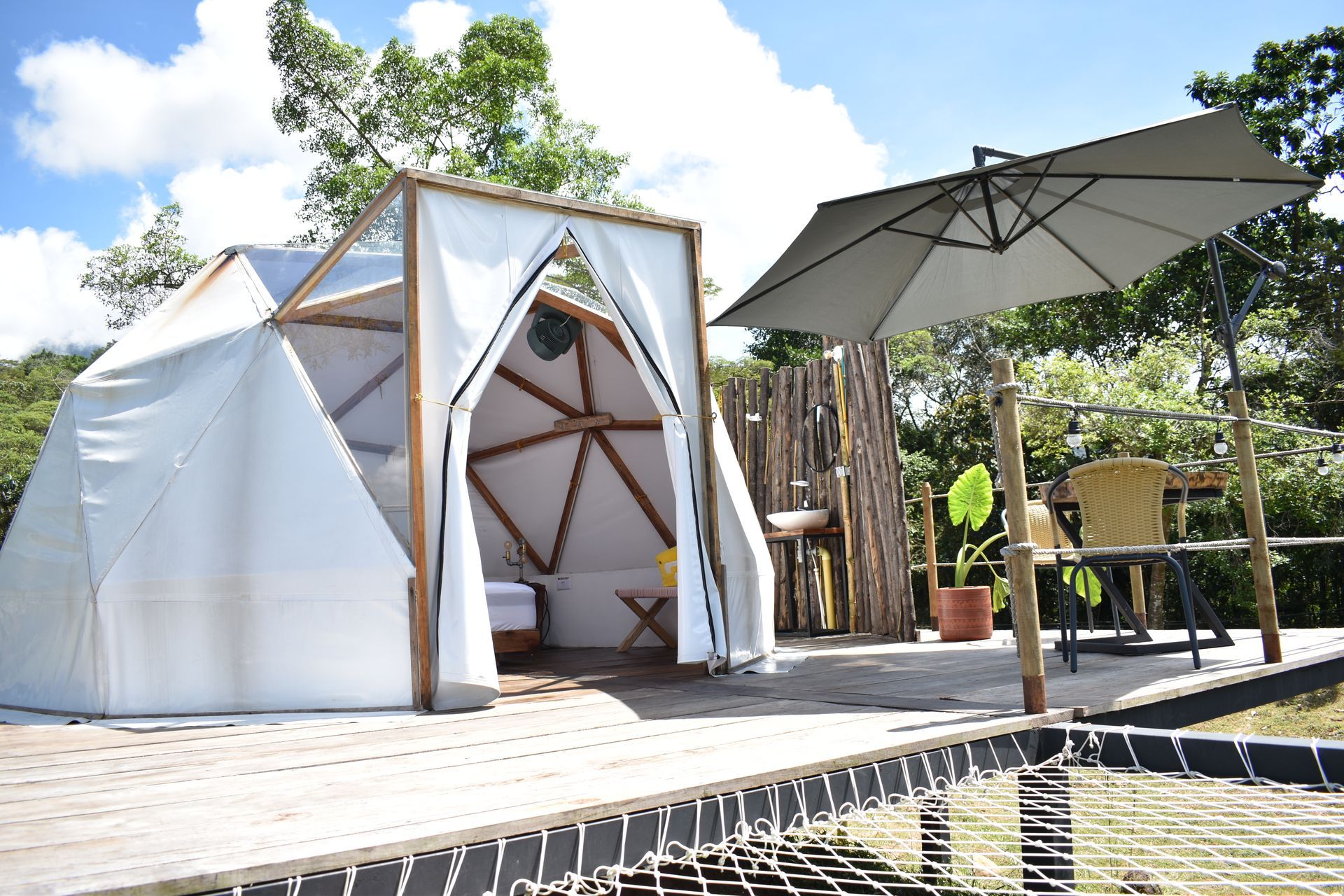 Un sitio de glamping con una tienda de campaña con domo geodésico, asientos al aire libre bajo una sombrilla y una hamaca.