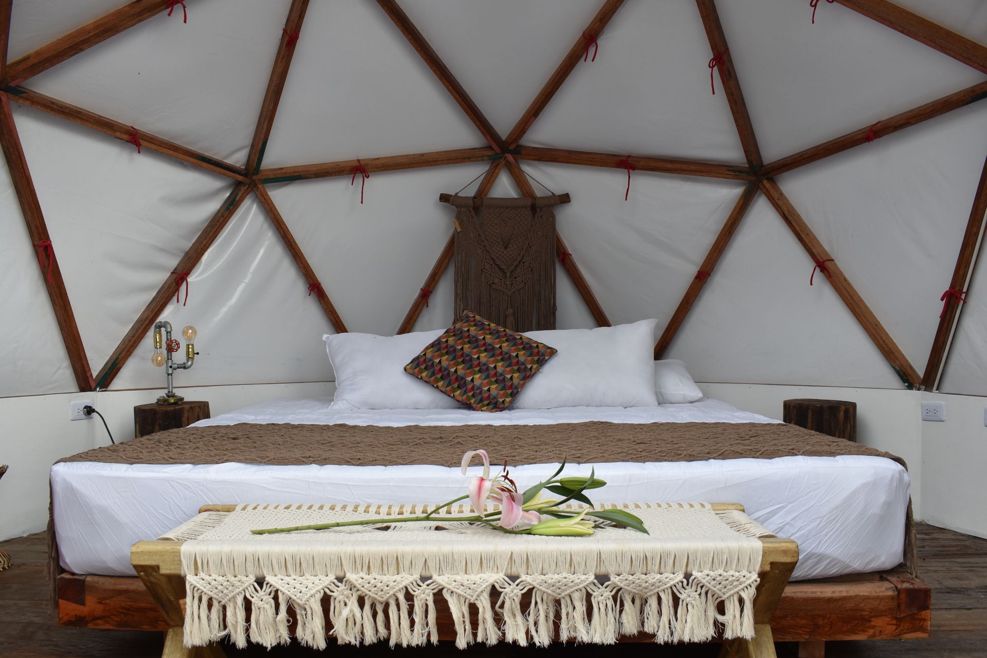 Interior de un dormitorio con cúpula geodésica con cama, mesa pequeña y detalles decorativos.