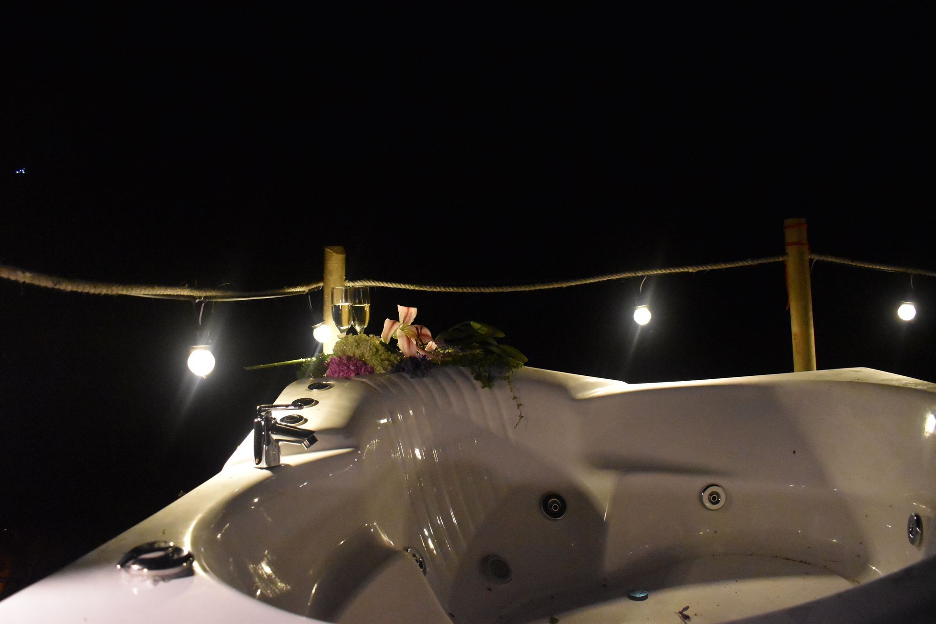 Jacuzzi blanco con decoración floral, iluminado por luces de cadena por la noche.