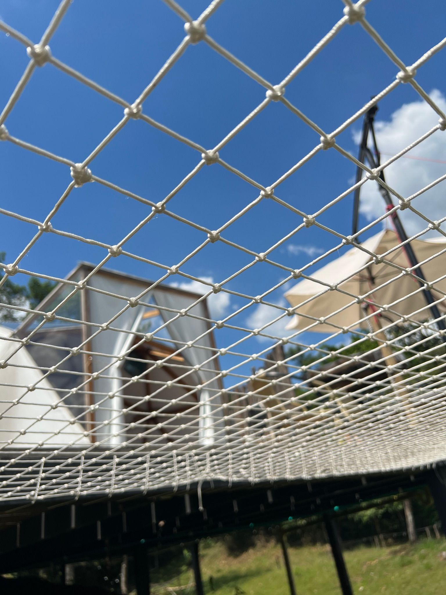 Red blanca frente a una estructura con una carpa blanca. Al fondo se ve una sombrilla y el cielo azul.