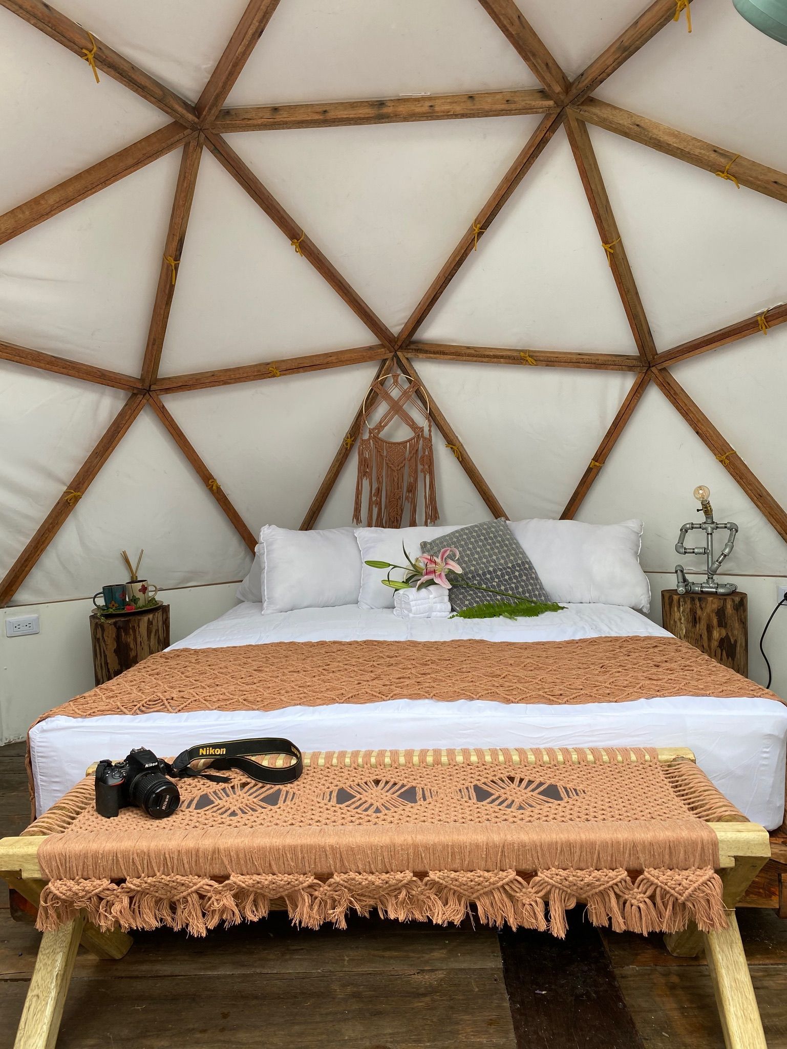 Acogedor dormitorio en una estructura abovedada. Ropa de cama blanca, colcha marrón y vigas de madera.