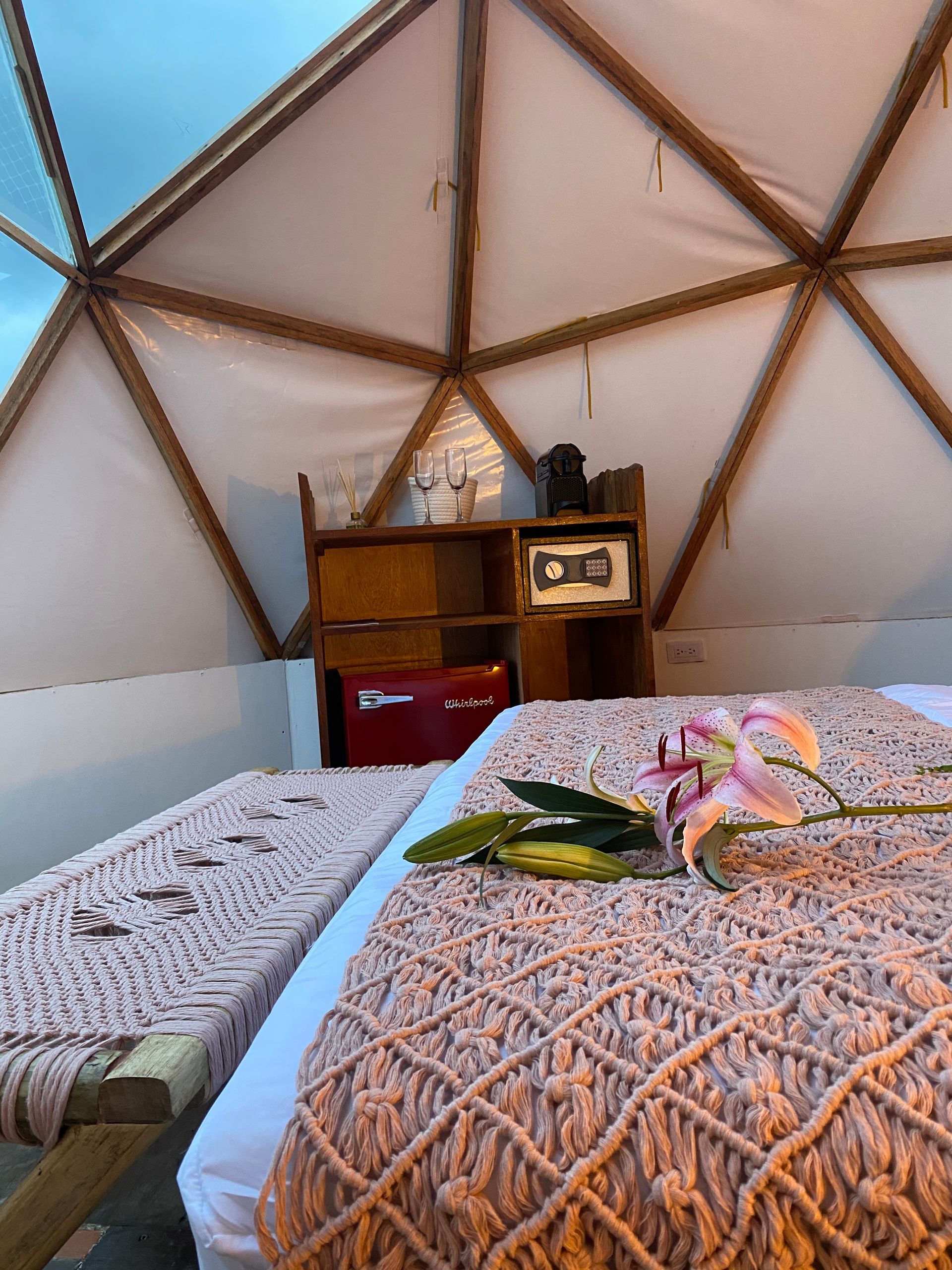 Acogedor interior en forma de cúpula con cama, manta de macramé, muebles y un lirio.