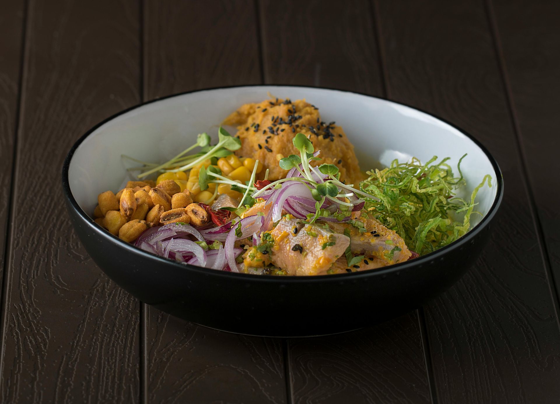 Tazón de comida colorida con salmón, maíz y brotes.