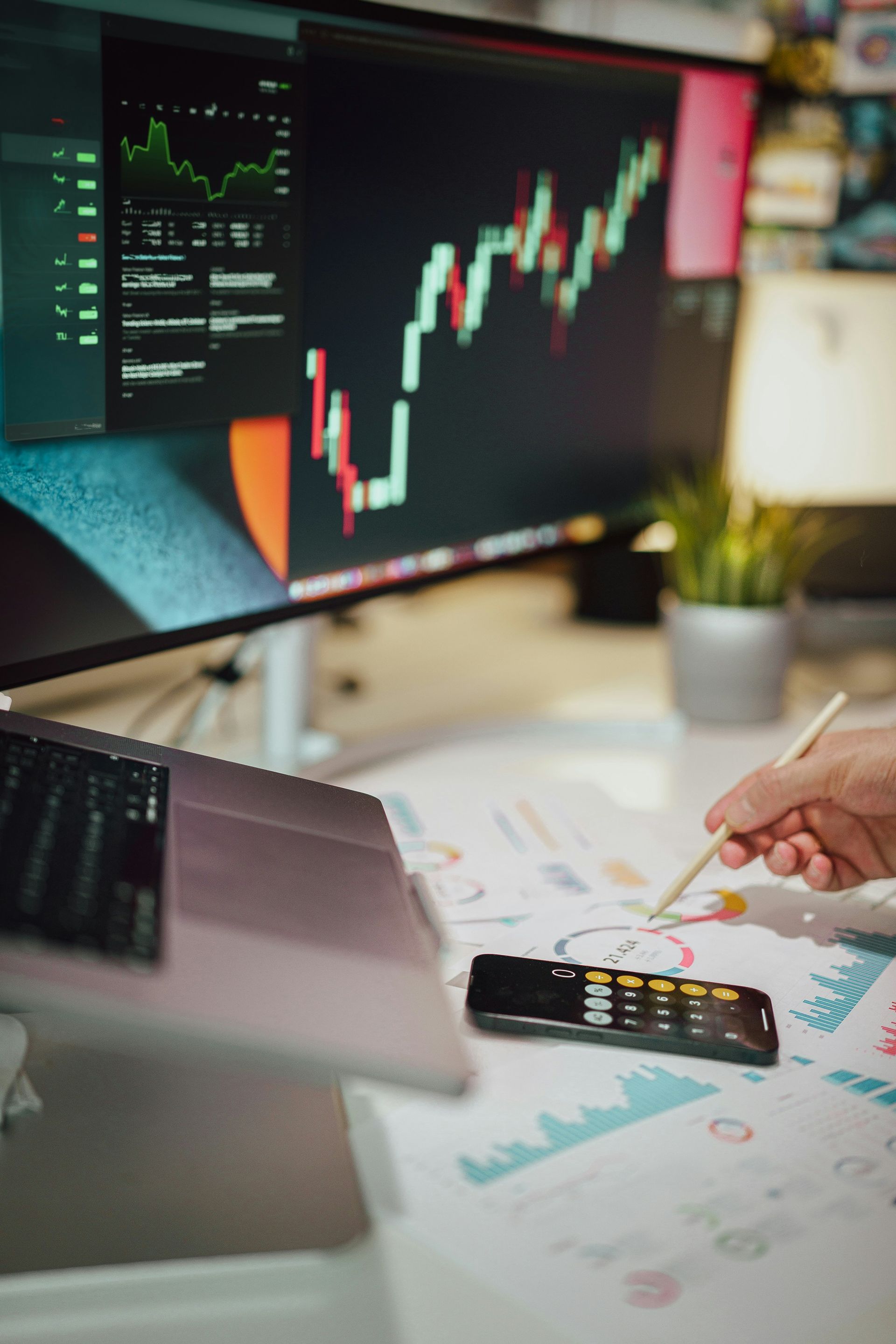 Person analyzing stock charts on a computer and paper with a pen.