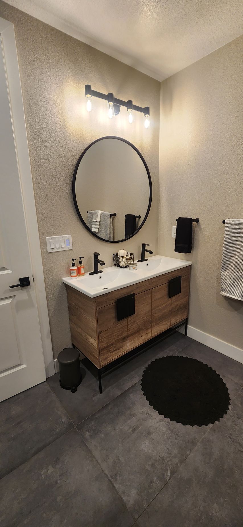 Bathroom with a wooden vanity, round mirror, and black accents.