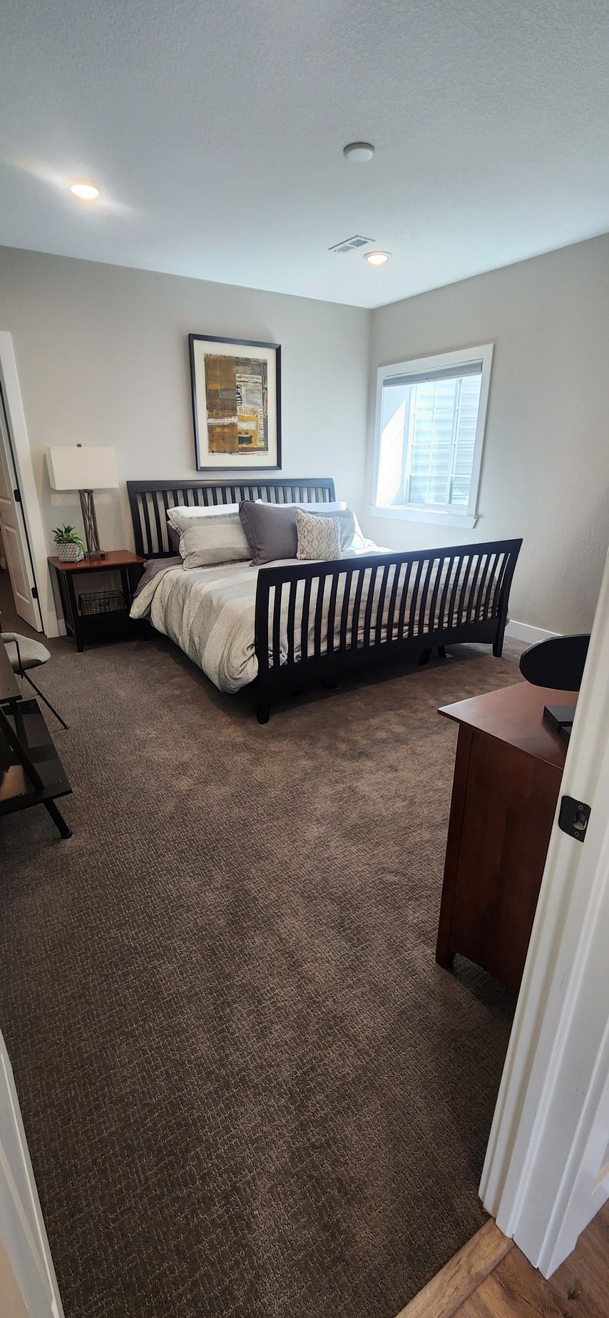 Bedroom with a black bed frame, gray bedding, and a brown carpet. Includes a wooden nightstand and dresser.