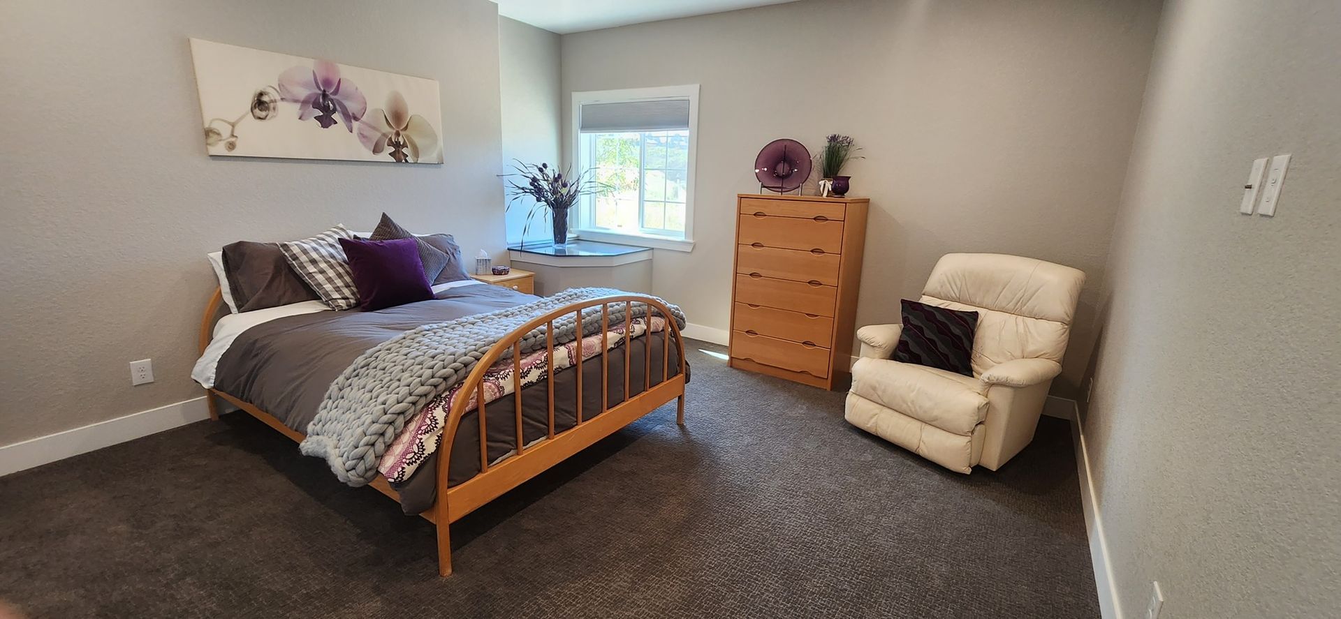 Bedroom with bed, dresser, recliner chair, and window. Gray walls and carpet.