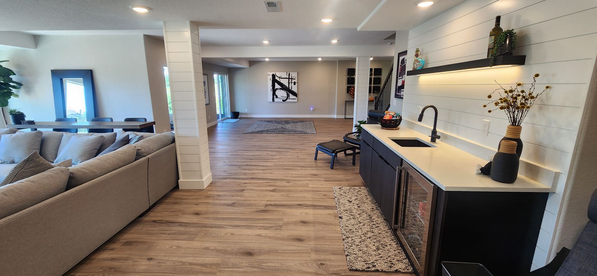Spacious interior with living area, bar, and artwork, featuring light wood floors and white walls.