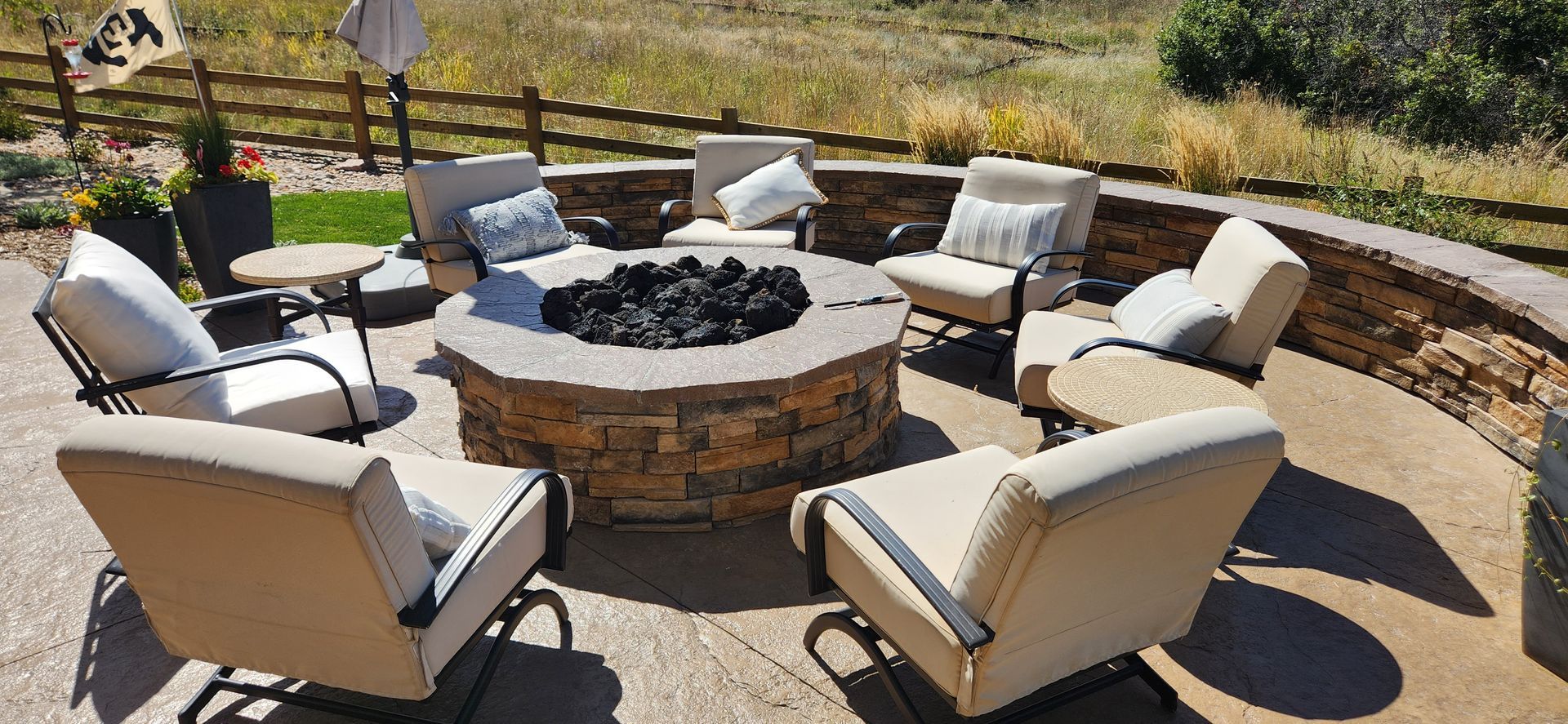 Patio with a stone fire pit surrounded by eight cushioned chairs on a sunny day.