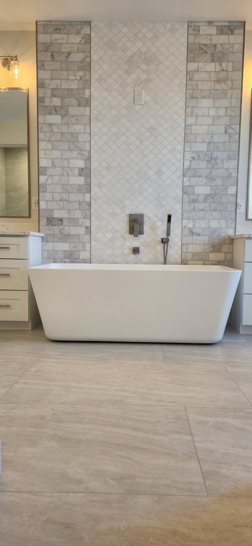 Freestanding white bathtub with tile backsplash in a modern bathroom.